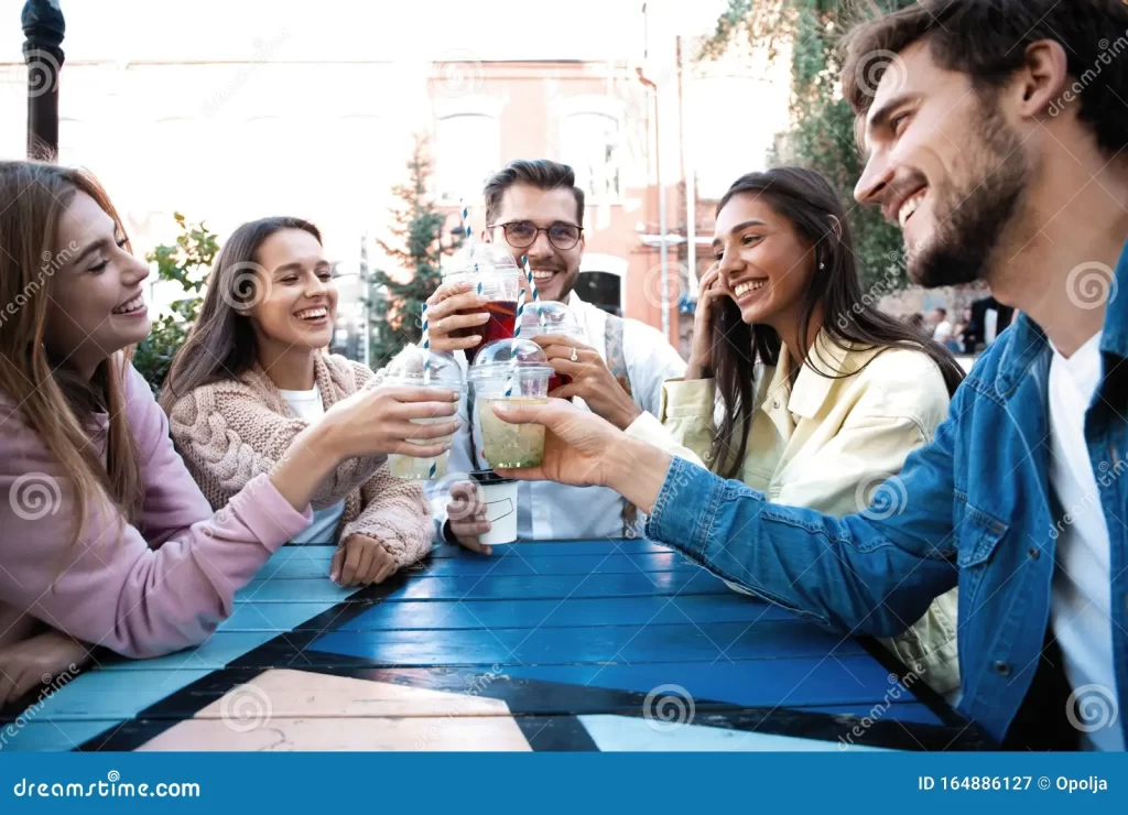 A group of Gen Z friends cheering with iced coffee and cold drinks at an outdoor table, illustrating modern beverage lifestyle trends.