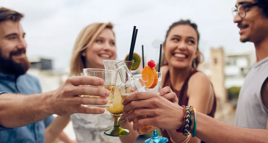 A group of diverse young adults smiling and clinking colorful beverage glasses outdoors, illustrating the social and community-driven nature of Gen Z beverage trends.